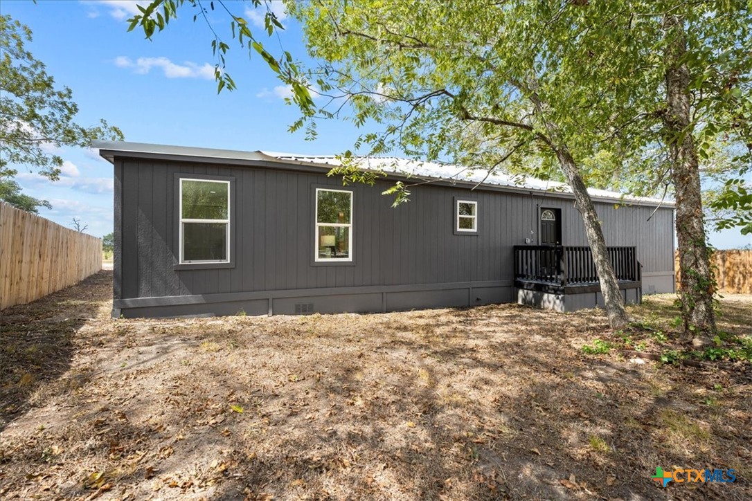 Charcoal-gray home with a metal roof and small entry porch beneath mature trees.