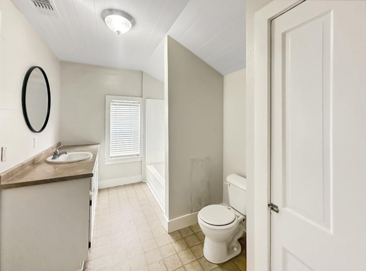 Bathroom with a brown vanity, oval mirror, bathtub behind a divider, and window with blinds.