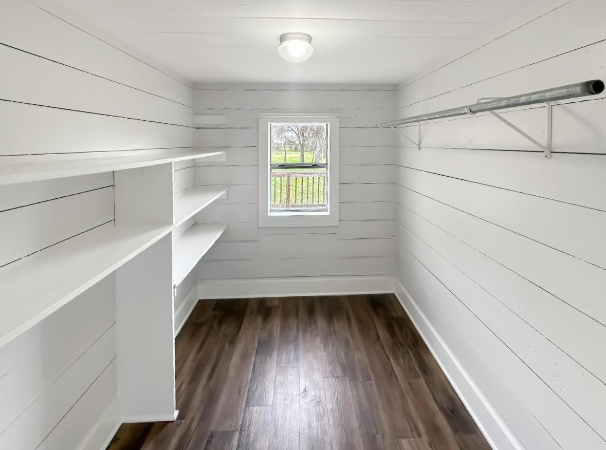 Walk-in closet with built-in white shelves, a clothes rod, and a window at the far end.