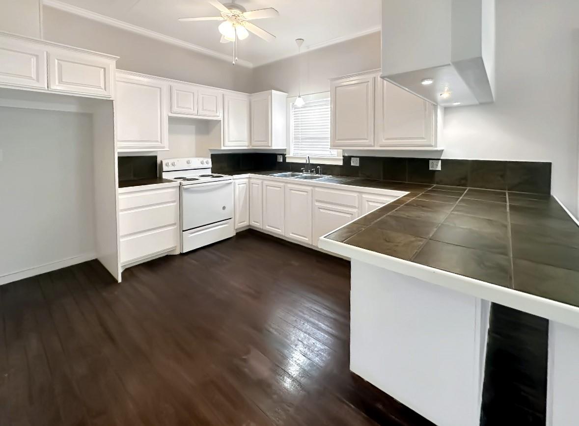 Kitchen with white cabinets, dark tile counters and backsplash, and dark wood flooring.