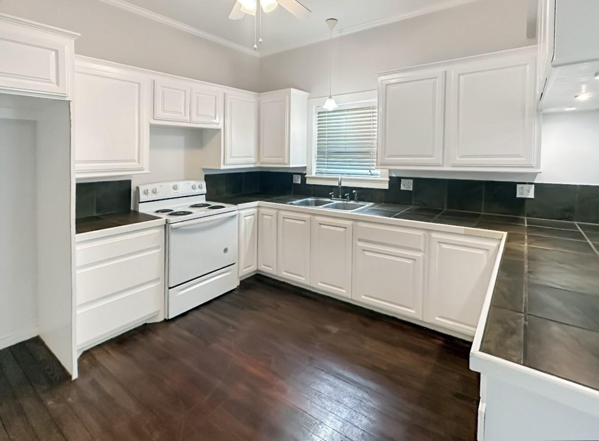 Kitchen with white cabinets, dark tile counters, an electric range, and dark wood floors.