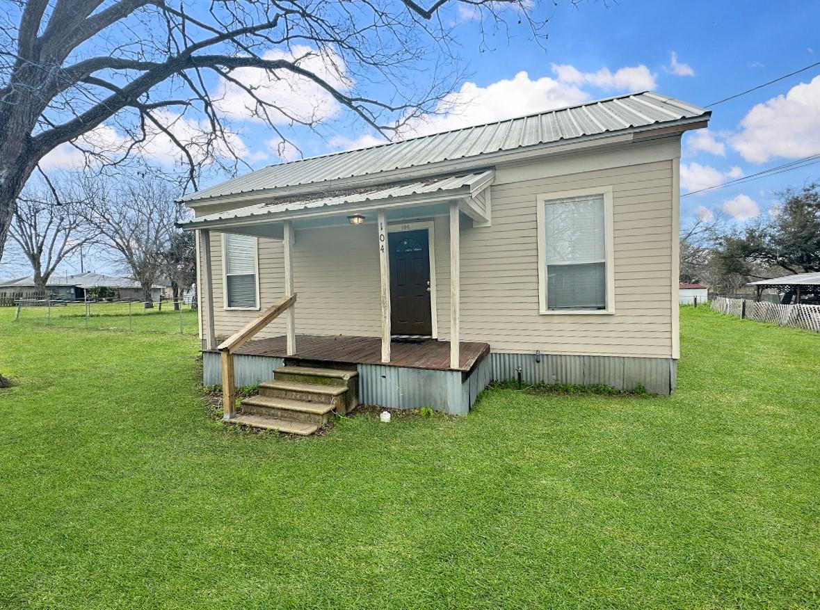 Small beige house with a metal roof, covered porch, and front steps on a green lawn.