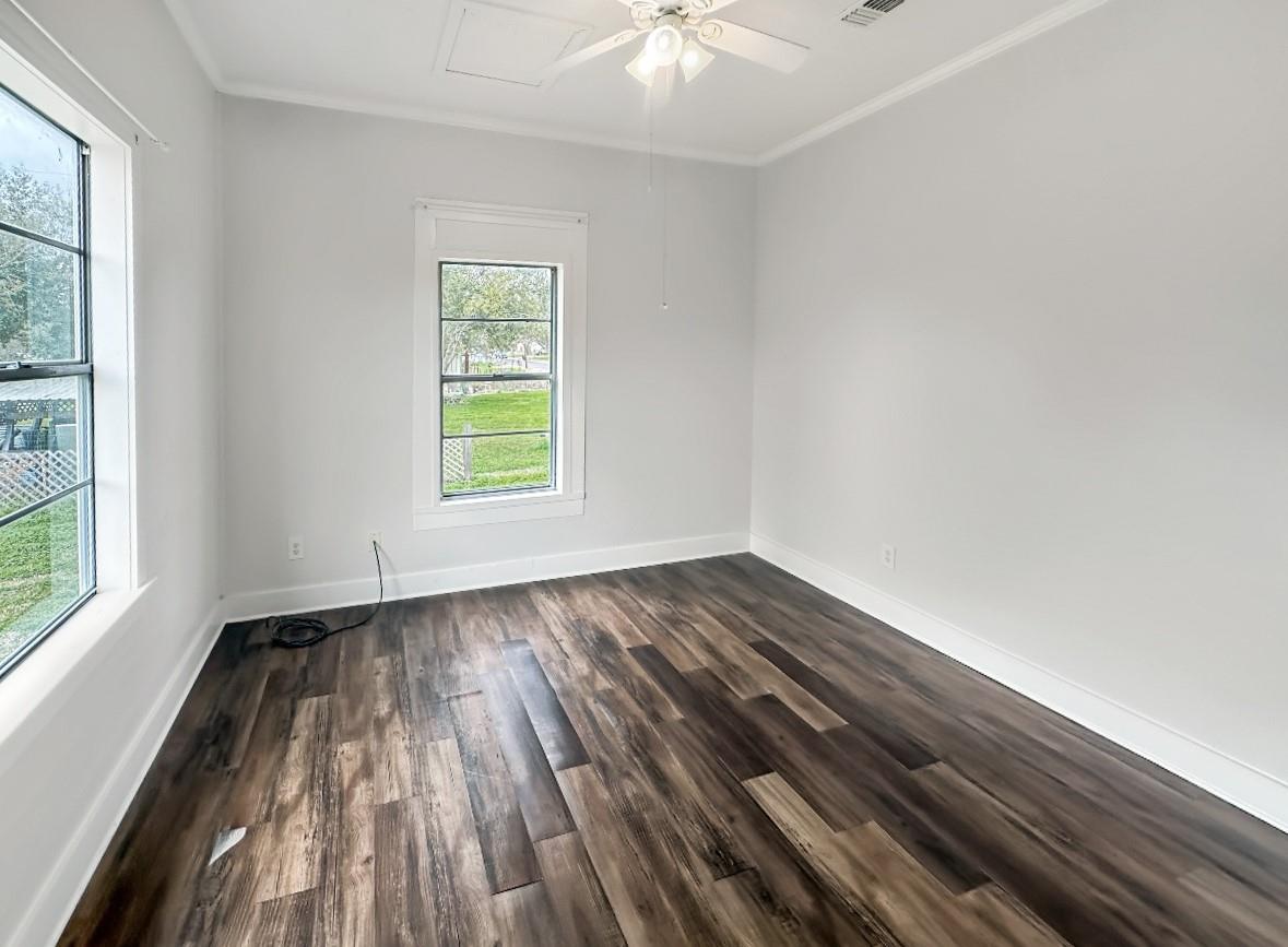 Empty room with dark plank flooring, two windows, and a ceiling fan.