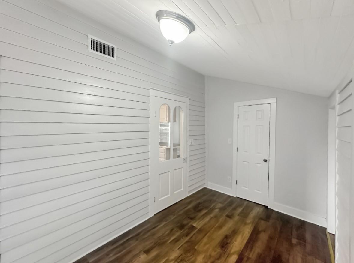 Vacant hallway with white plank walls, dark wood-look flooring, and a glass-paneled interior door.