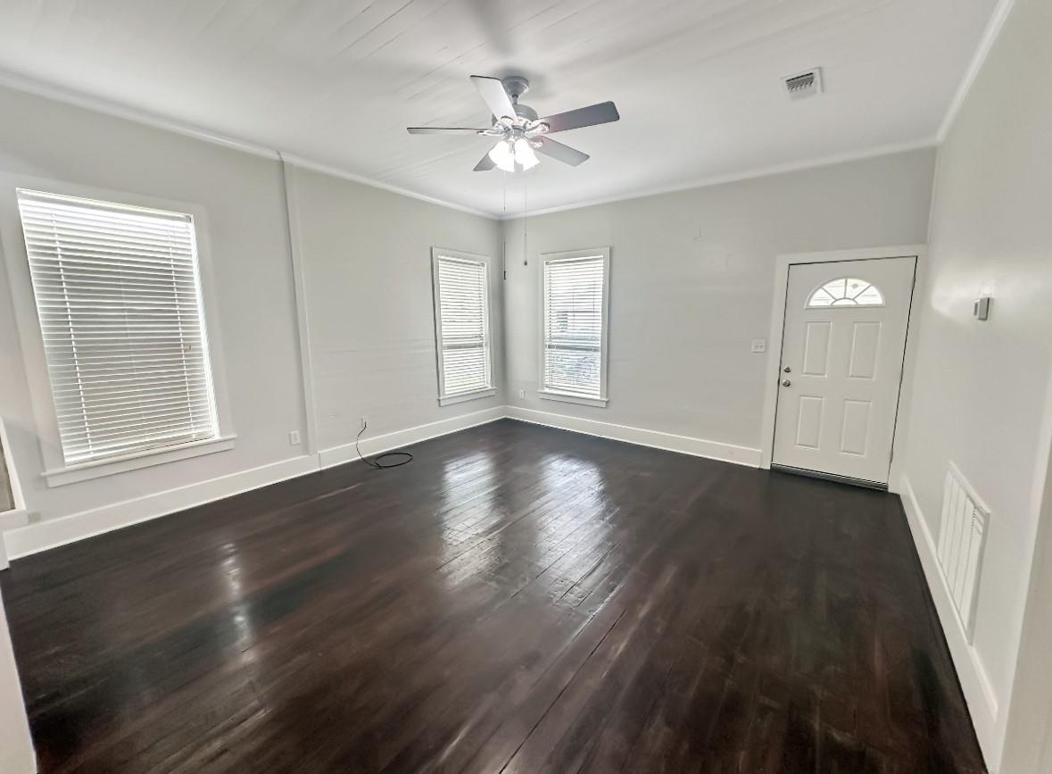 Empty room with dark hardwood floors, a ceiling fan, several windows, and an exterior door.