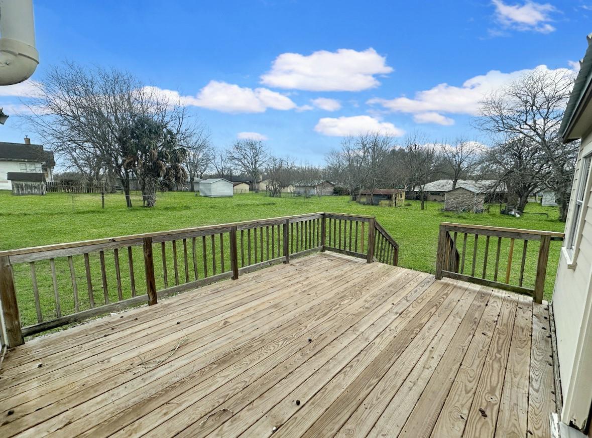 Wooden deck overlooking a green lawn, outbuildings, and leafless trees.