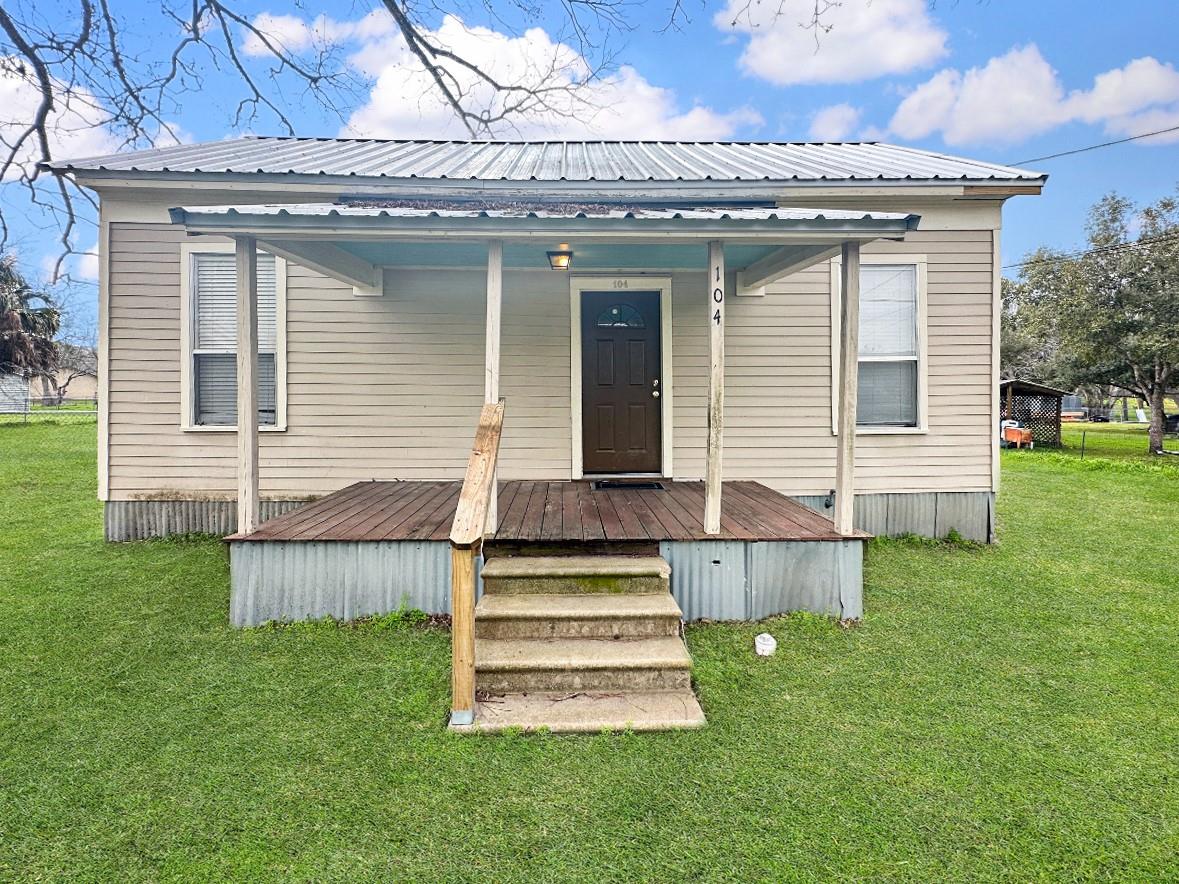 Small beige house with a metal roof, covered porch, and concrete front steps.