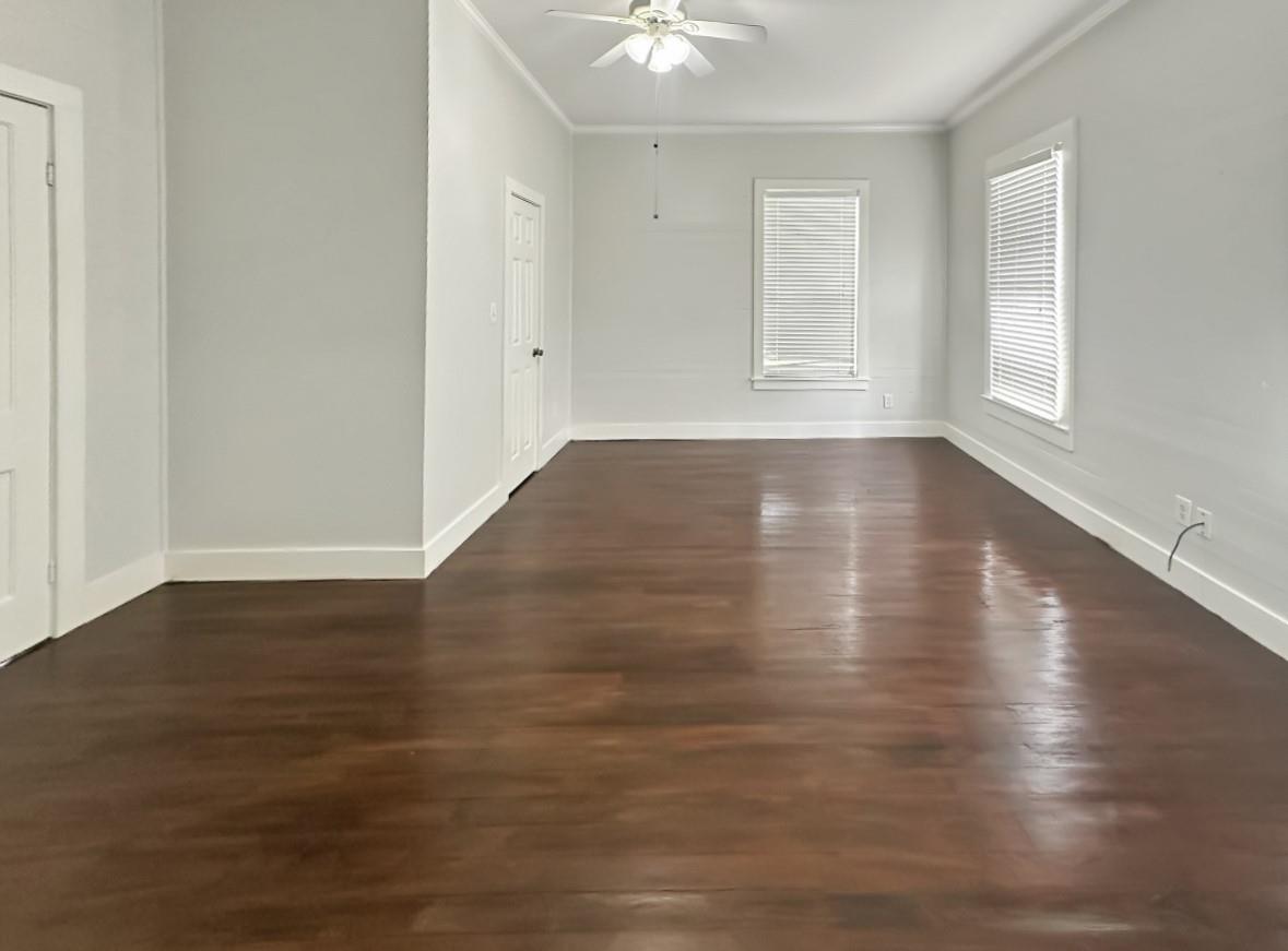 Empty room with polished hardwood floors, two blind-covered windows, and a ceiling fan.