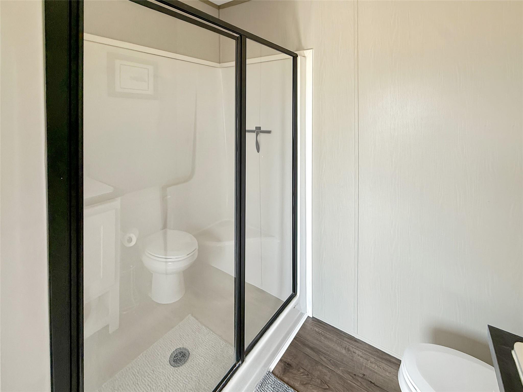 Bathroom with a glass-enclosed shower, white toilet, and wood-look flooring.