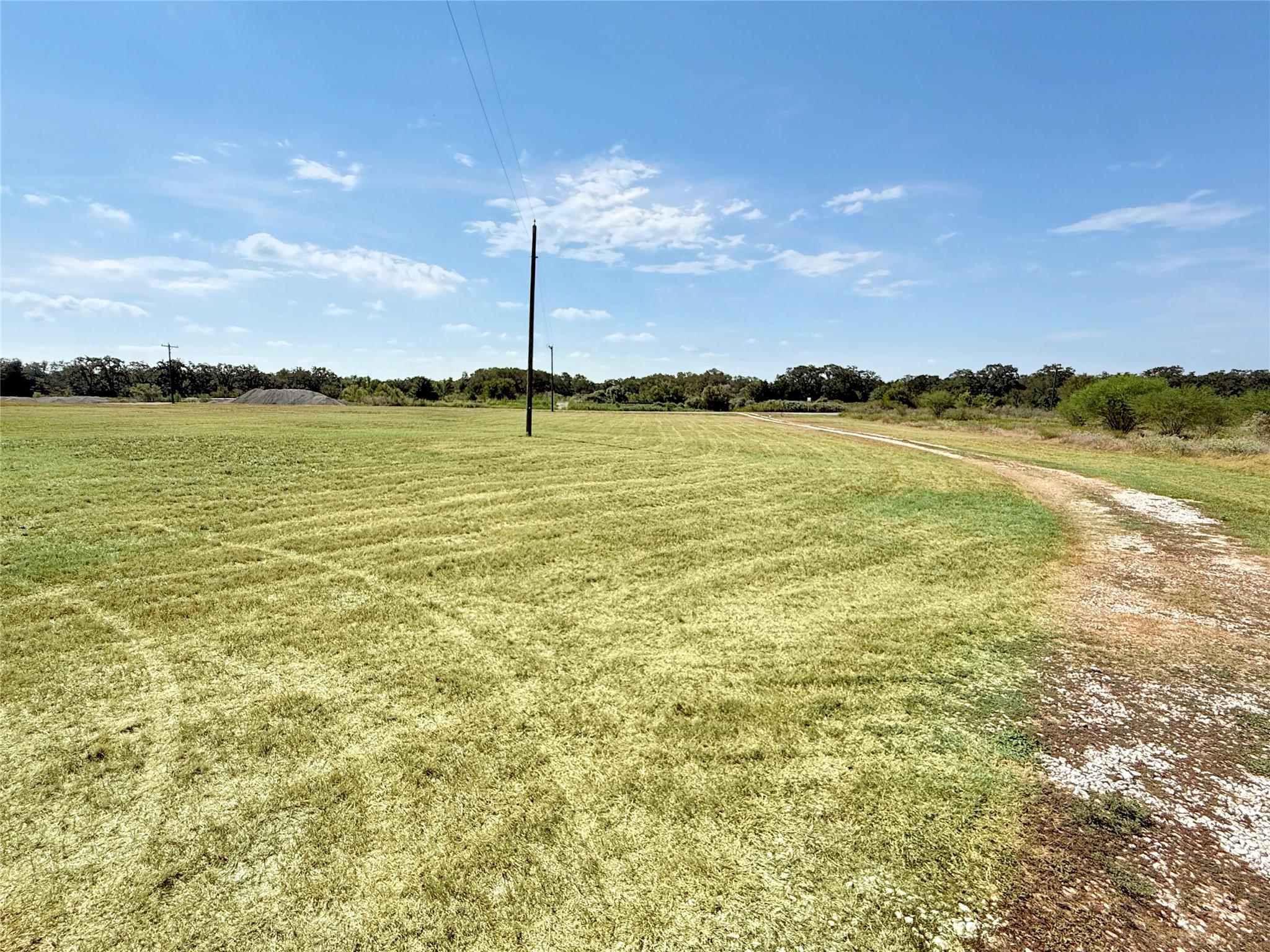 Cleared grassy lot with a curving gravel drive, utility poles, and distant trees.