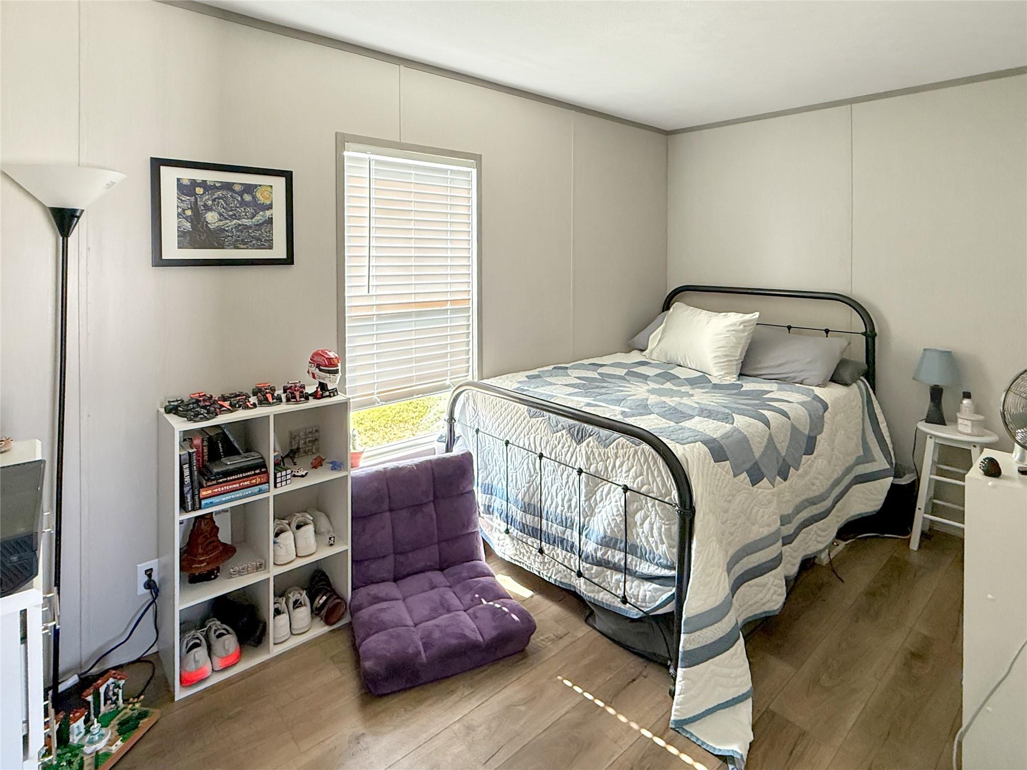 Bedroom with a black metal bed, blue-and-white quilt, purple floor chair, and window with white blinds.