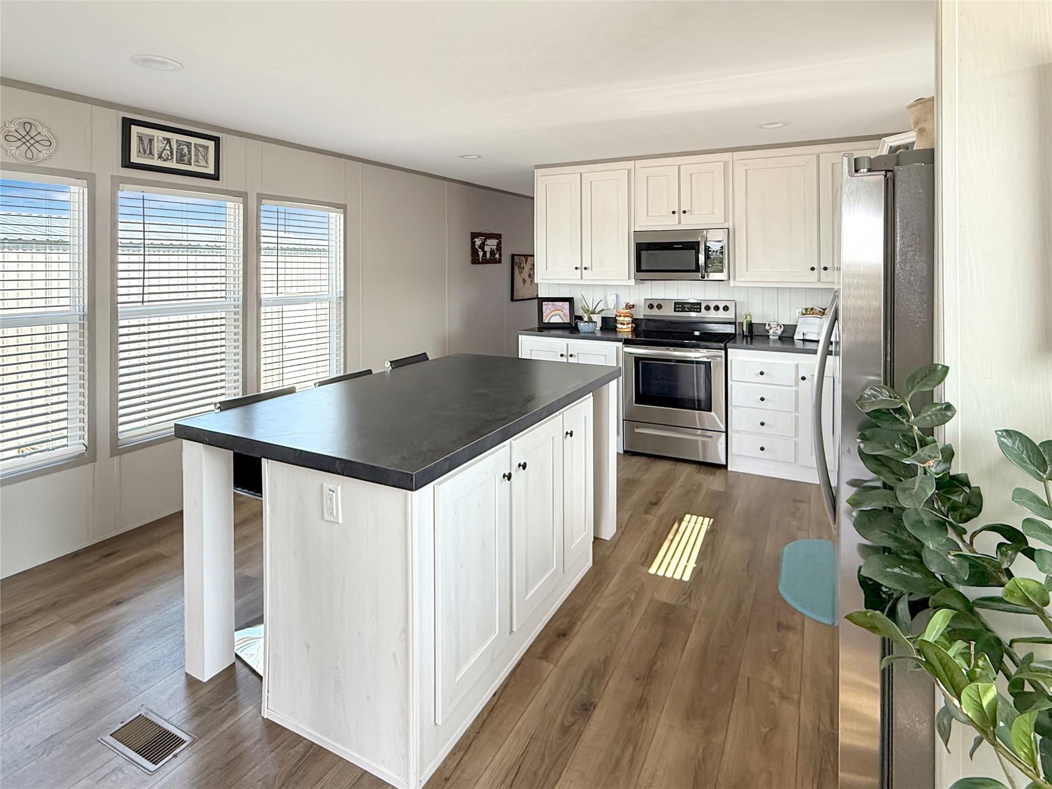Bright kitchen with a large dark-countertop island, white cabinets, and stainless steel appliances.