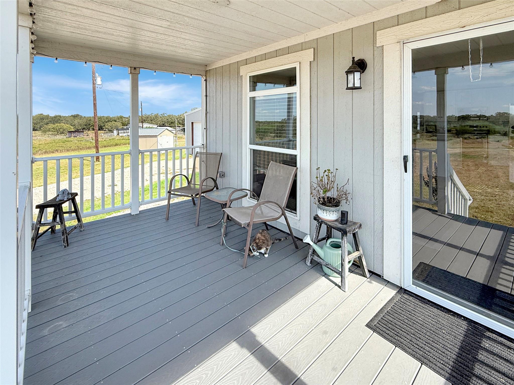 Covered porch with two chairs and a cat, overlooking a rural yard.