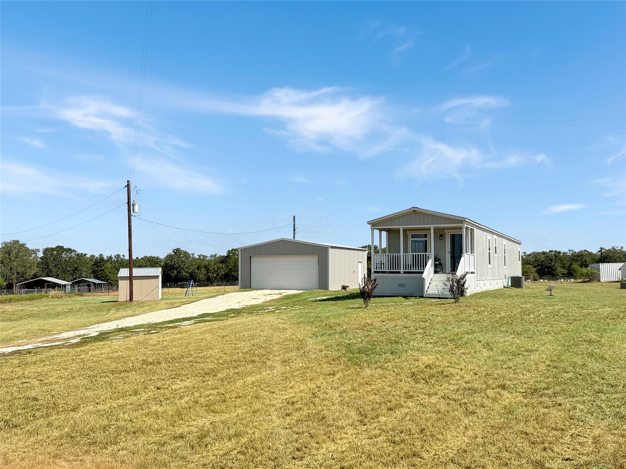 Manufactured home with a covered porch, detached garage, and shed on a grassy lot.