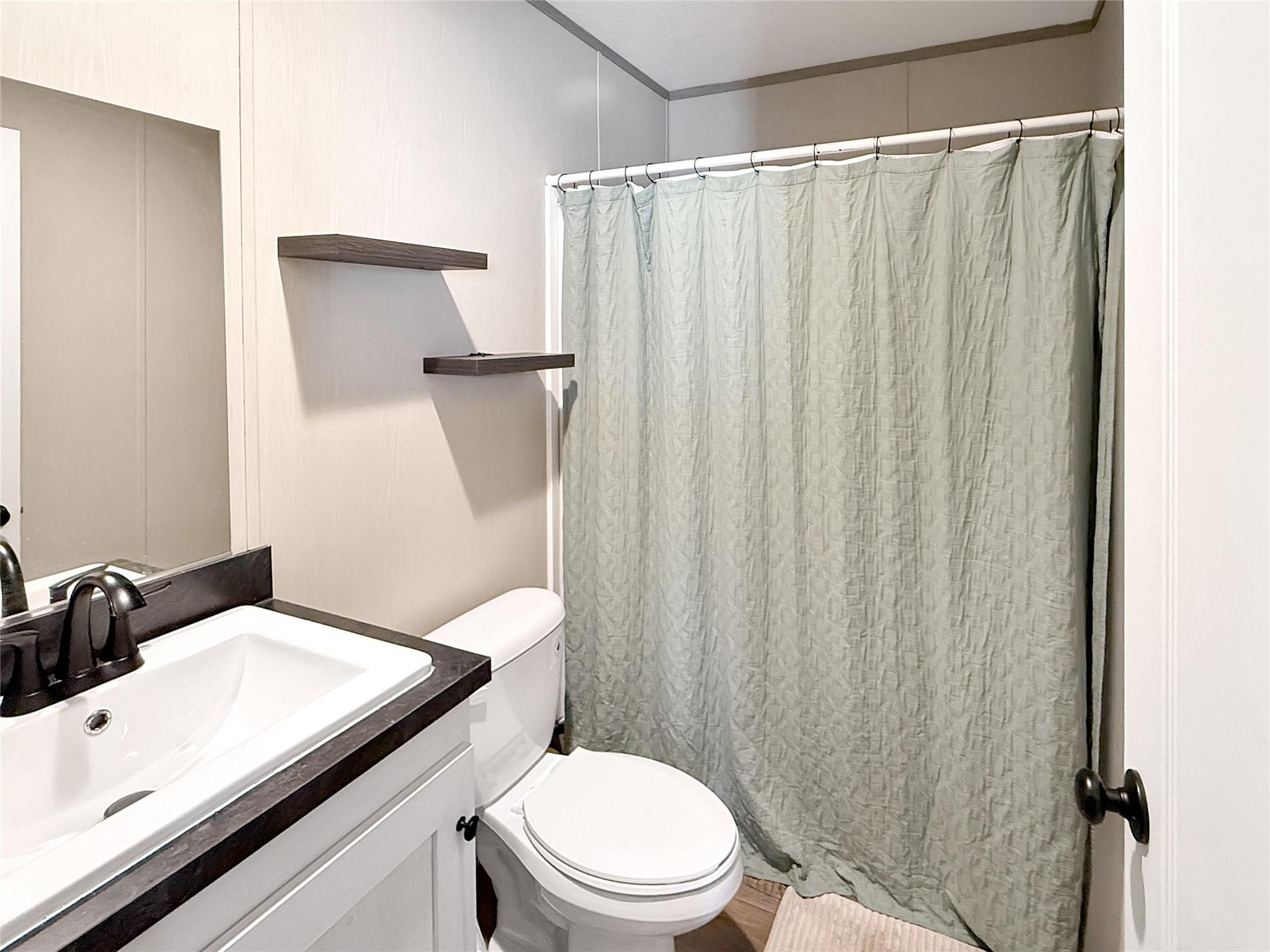 Bathroom with a dark-countertop vanity, white toilet, and gray shower curtain.