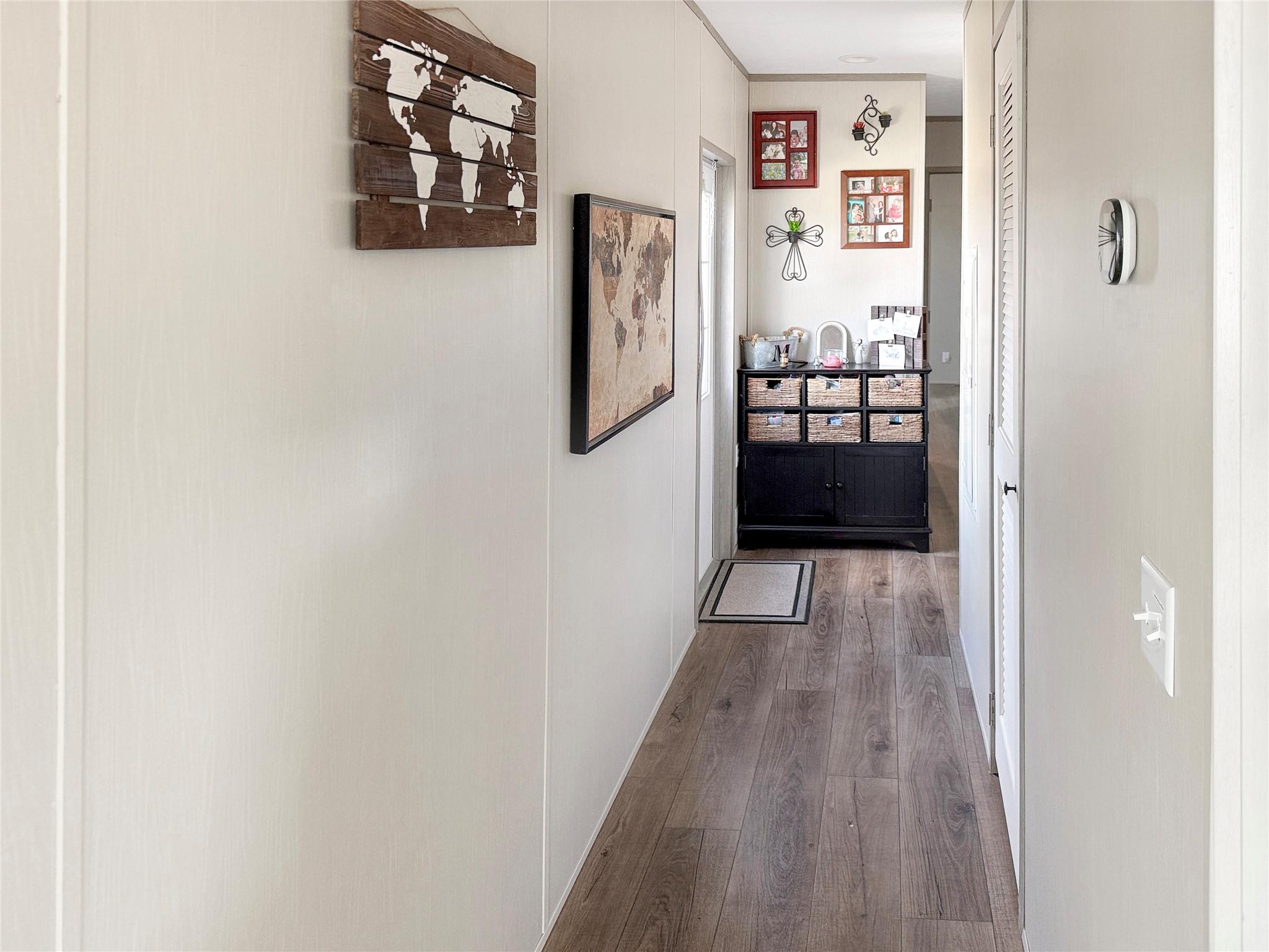 Hallway with wood-look flooring, world map wall art, and a dark cabinet with wicker baskets.