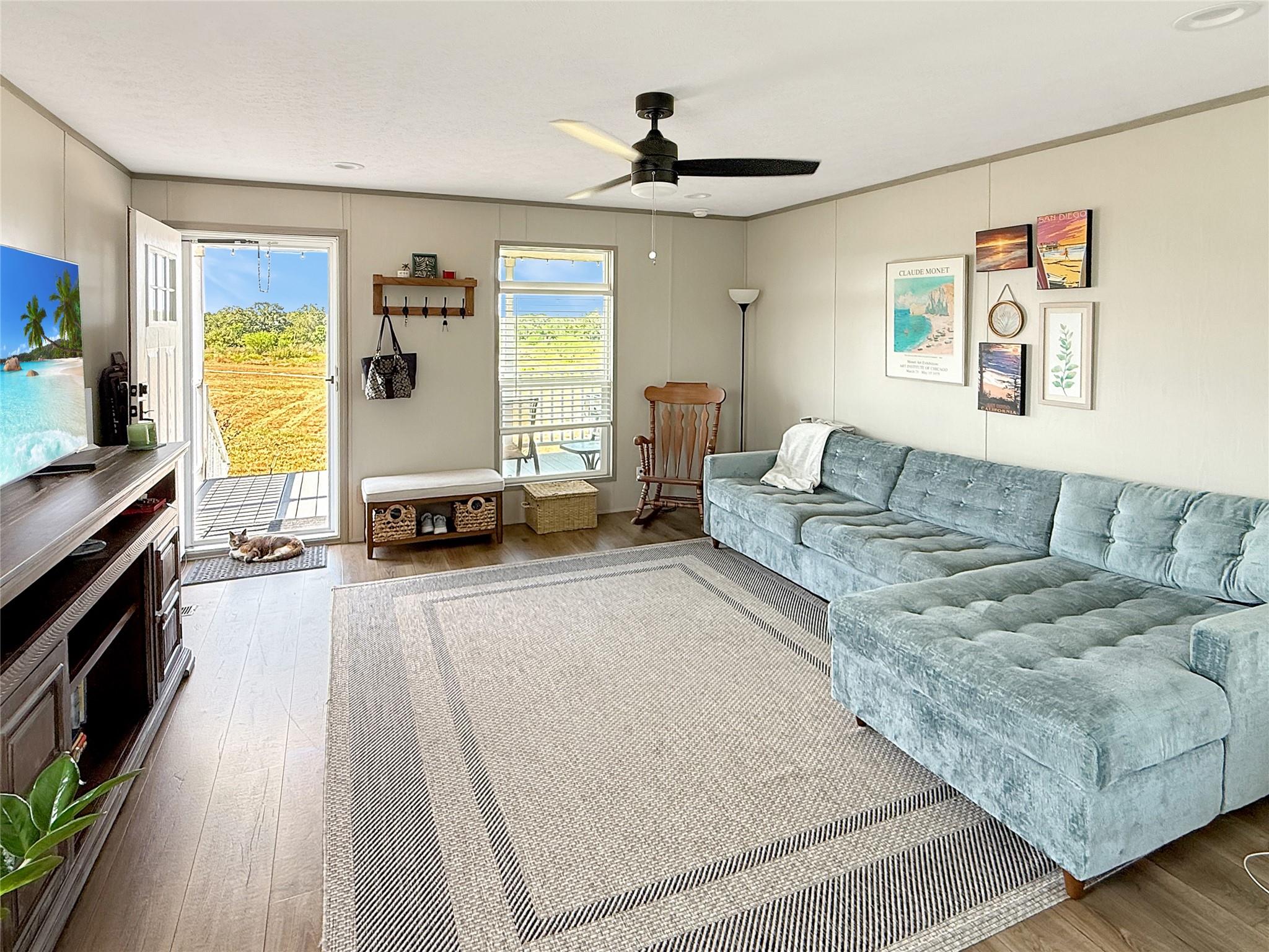 Living room with a pale blue sectional, patterned rug, and open door overlooking a sunny field.
