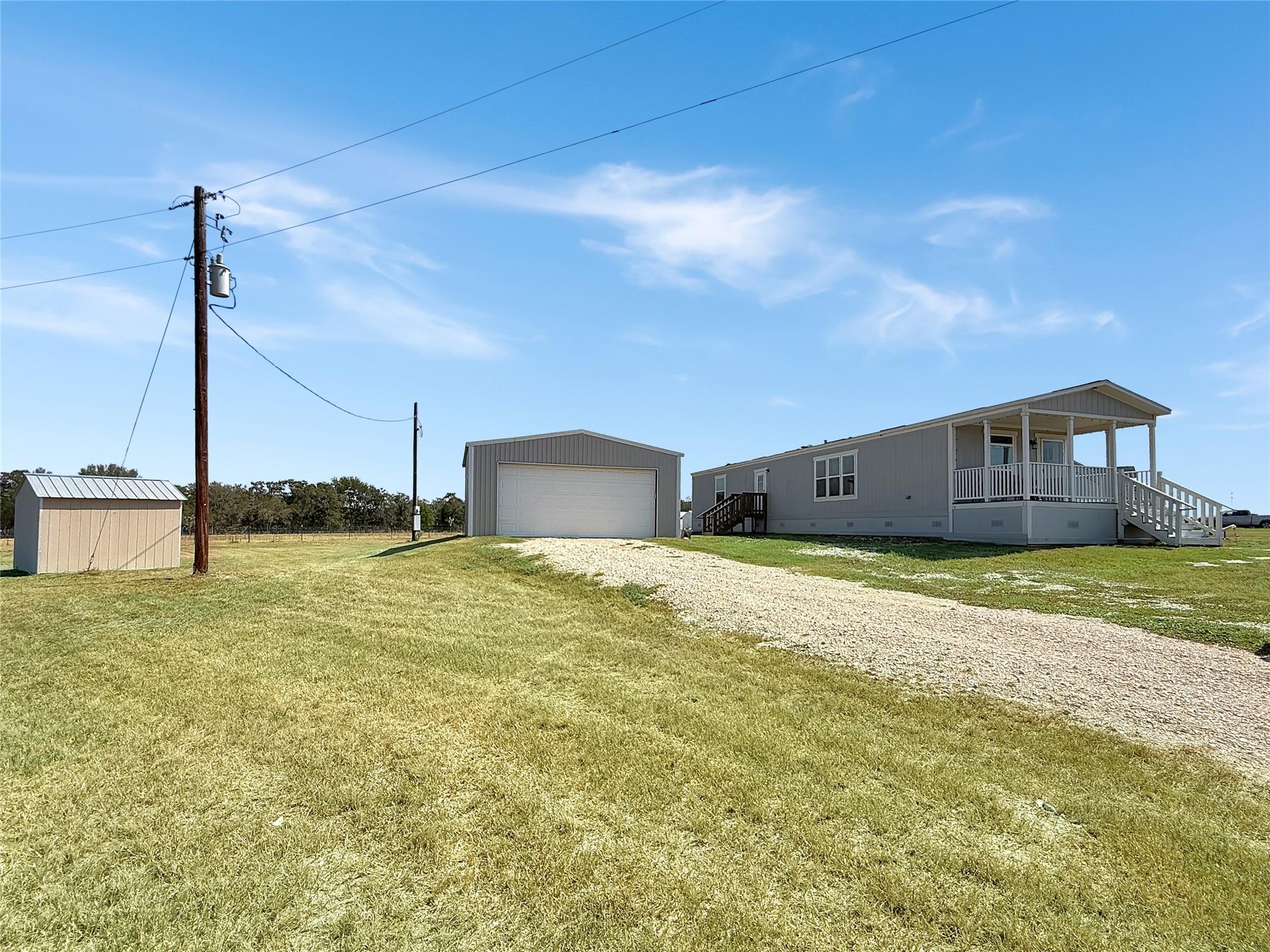 Gray home with a covered porch, detached garage, small shed, and gravel driveway on a grassy lot.