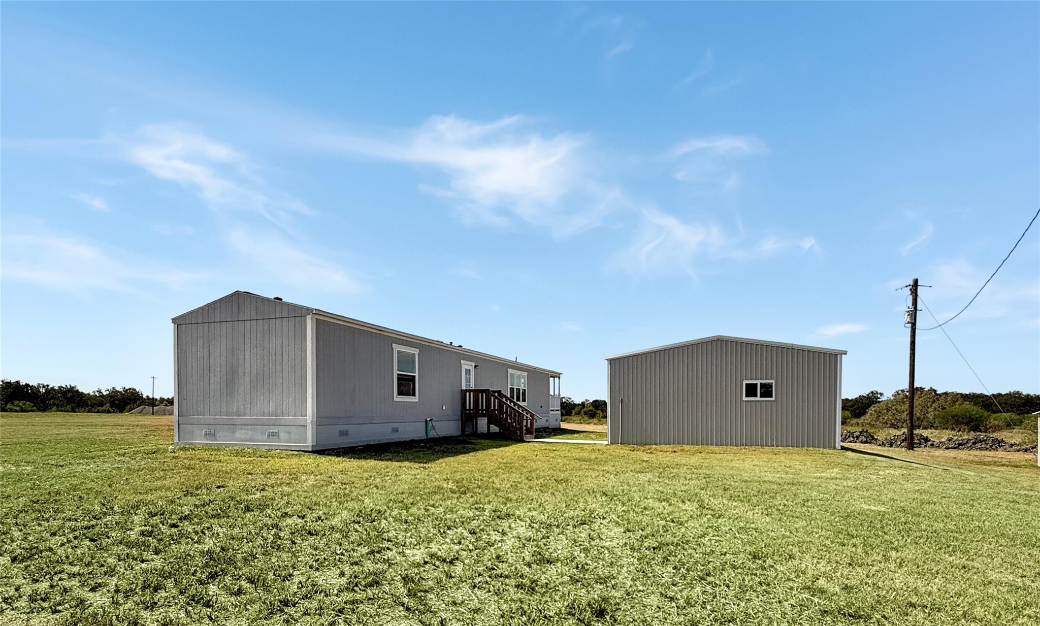 Gray manufactured home and detached metal outbuilding on a broad grassy lot.