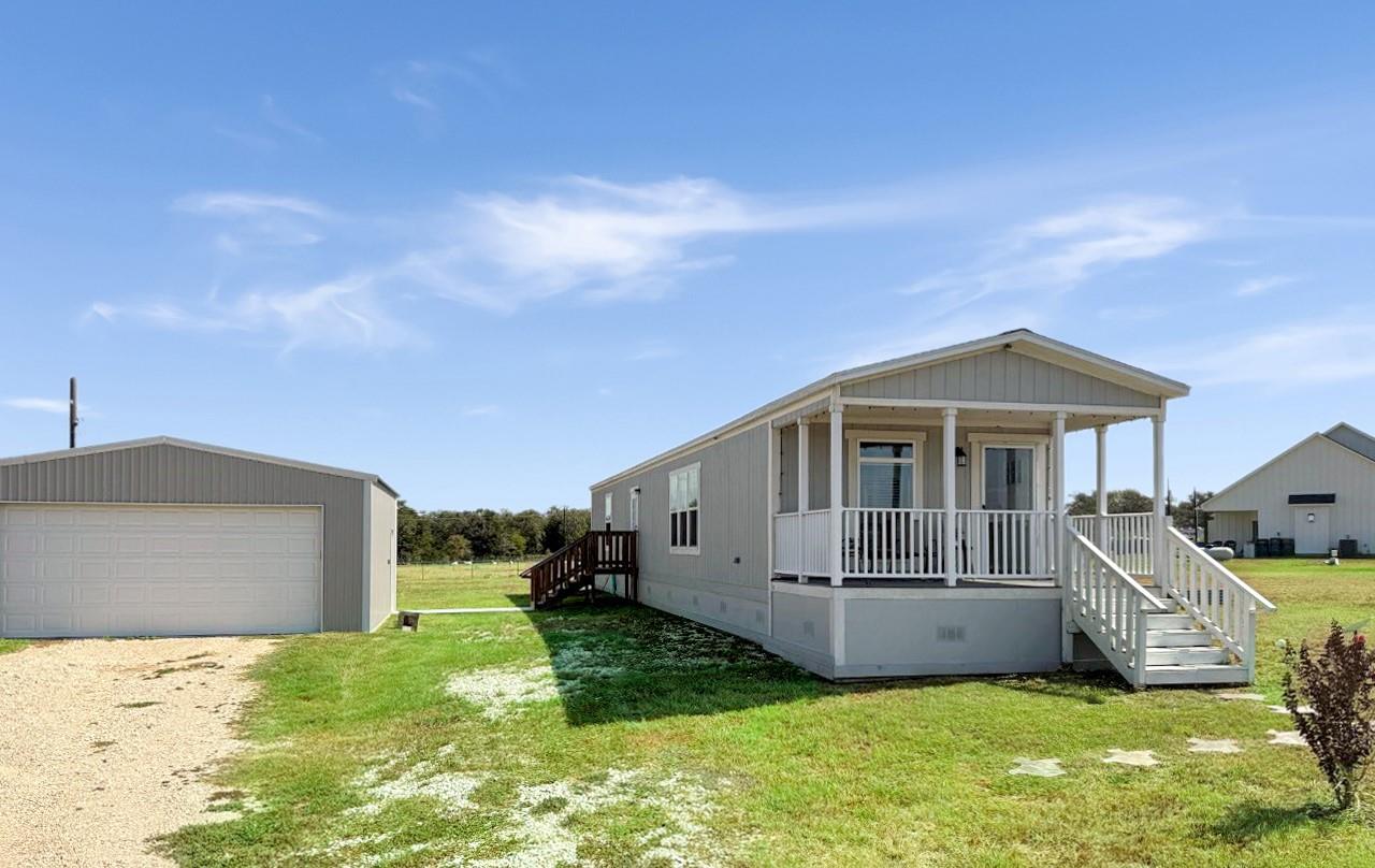 Manufactured home with a covered front porch beside a detached garage and grassy yard.