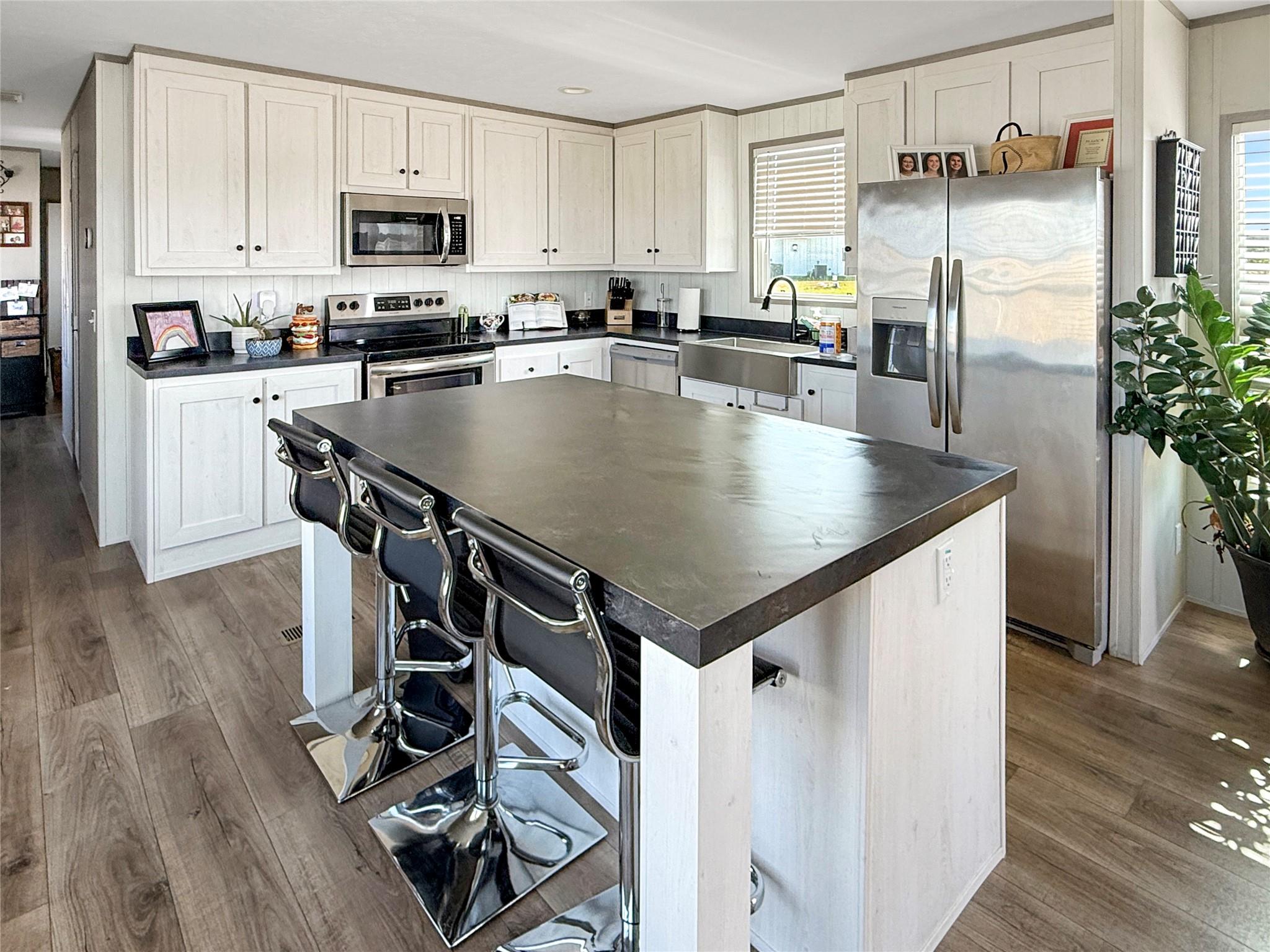Kitchen with a large island and bar stools, white cabinets, dark counters, and stainless steel appliances.