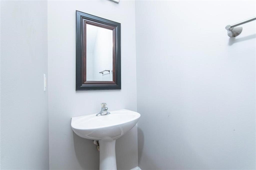 Bathroom pedestal sink with chrome faucet, dark-framed mirror, and wall-mounted towel bar.