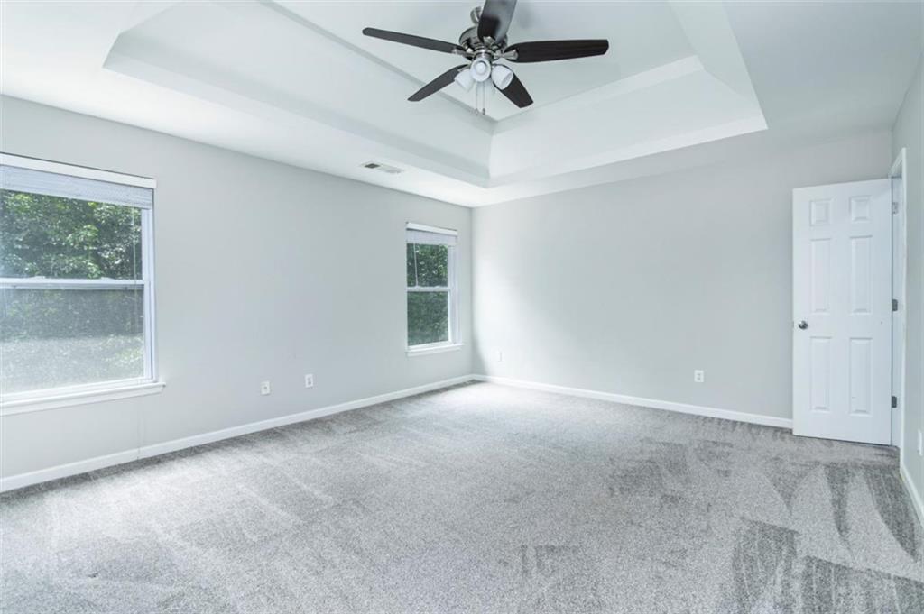 Empty carpeted bedroom with two windows and a tray ceiling fan.