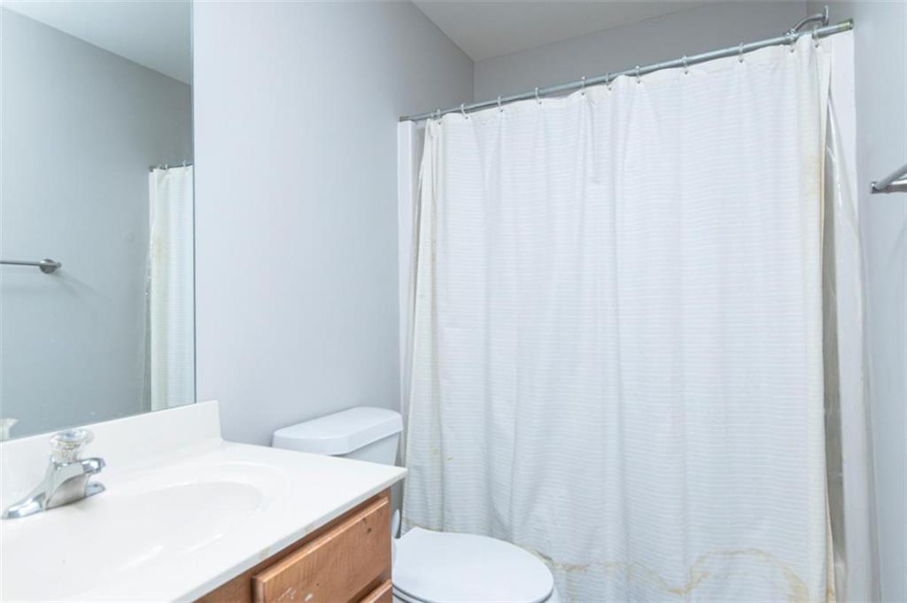Bathroom with a wood vanity, white sink, toilet, and white shower curtain.