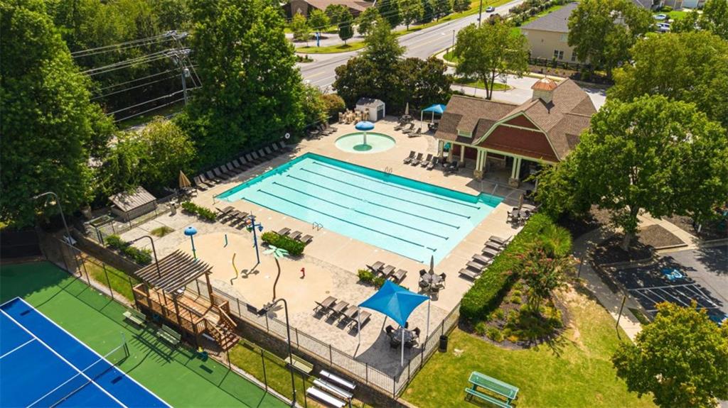 Aerial view of a community pool and tennis courts beside a clubhouse and splash pad.