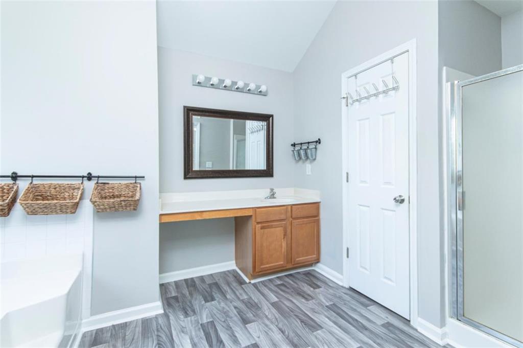 Bathroom with a wood vanity, gray plank flooring, wall-mounted baskets, and a glass shower enclosure.