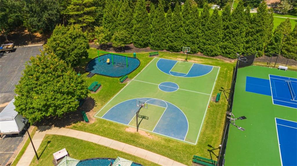 Aerial view of community basketball and tennis courts beside a playground and tree-lined lawn.
