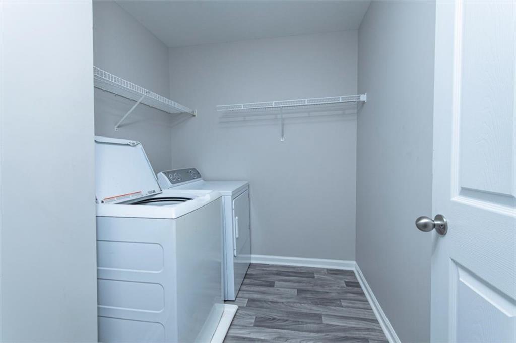 Laundry room with a top-loading washer and dryer beneath wire shelves.