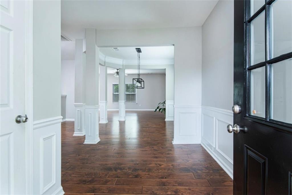 Entryway with dark hardwood floors, white paneled walls, decorative columns, and a black glass-paneled front door.