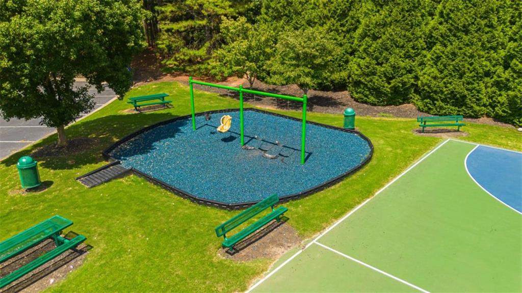 Outdoor playground with green swings beside a sport court and benches, viewed from above.