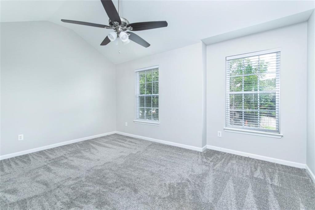 Empty bedroom with gray carpet, two windows, and a ceiling fan.