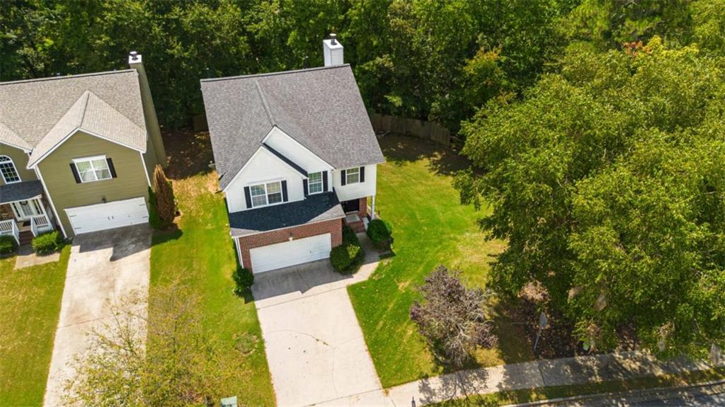 Aerial view of a two-story white-and-brick house with a front garage, driveway, and tree-lined lawn.