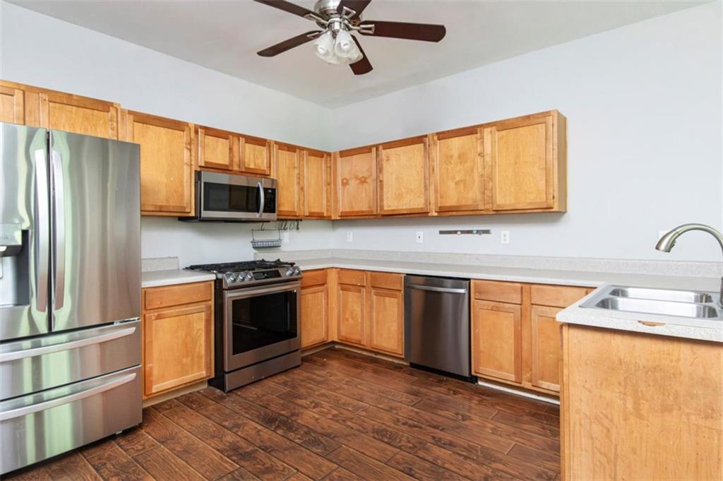Kitchen with honey-colored wood cabinets, stainless steel appliances, and dark wood-look flooring.