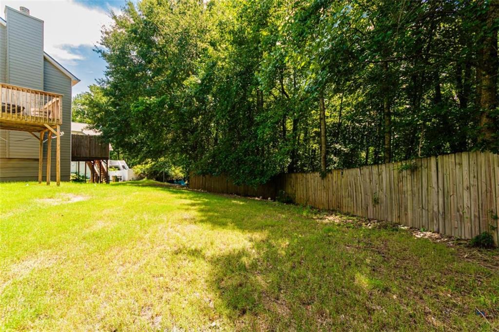 Backyard lawn bordered by a wooden fence and mature trees, with a raised deck beside the house.