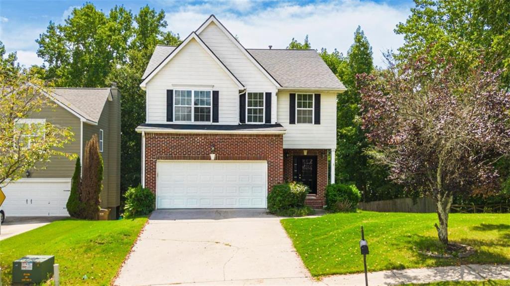 Two-story white-and-brick house with black shutters, attached garage, and wide driveway.