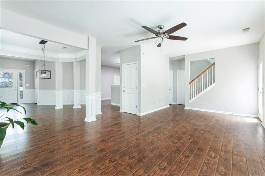 Open, vacant living area with dark wood floors, decorative columns, and a staircase.