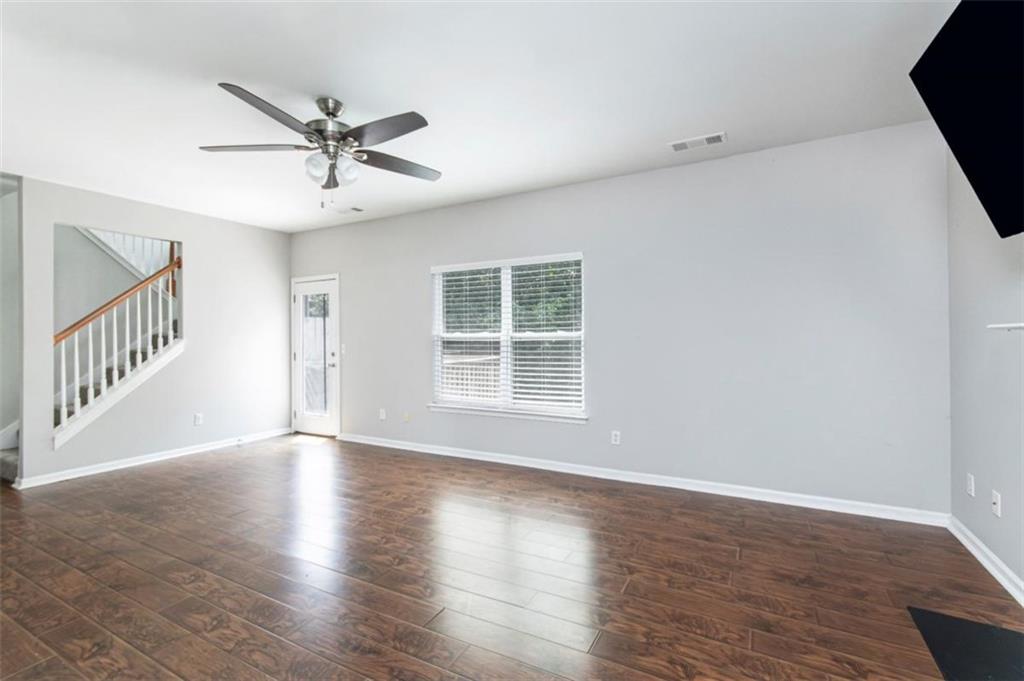 Empty living room with dark wood-look floors, a ceiling fan, and a staircase.