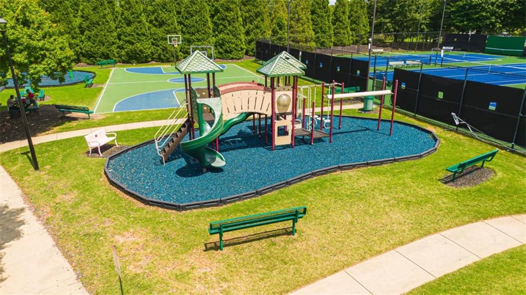 Community playground with blue safety surfacing beside tennis and basketball courts.