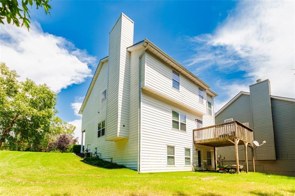 Rear of a multi-story house with a raised wooden deck overlooking a green lawn.