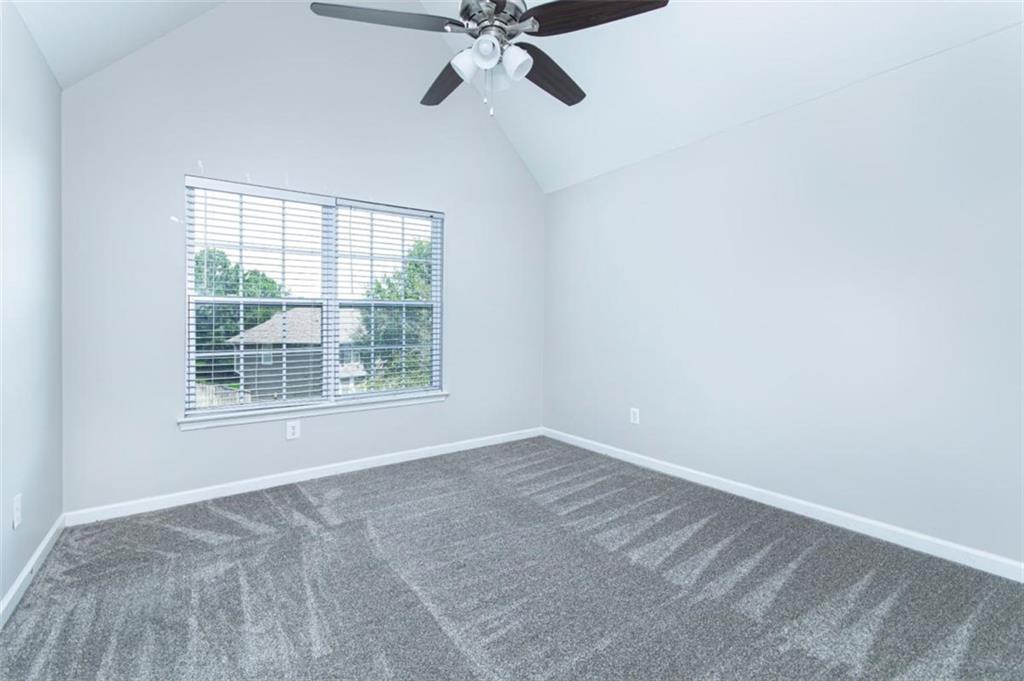 Empty bedroom with gray carpet, vaulted ceiling, ceiling fan, and a wide window with blinds.