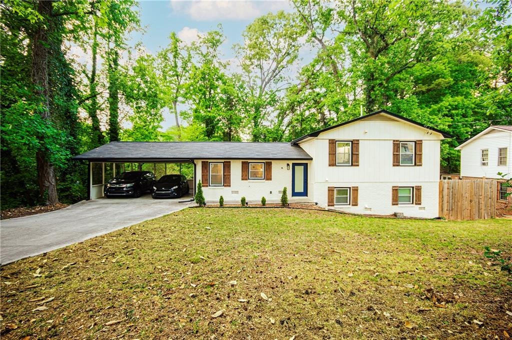 White split-level home with a covered carport, two parked cars, and mature trees.