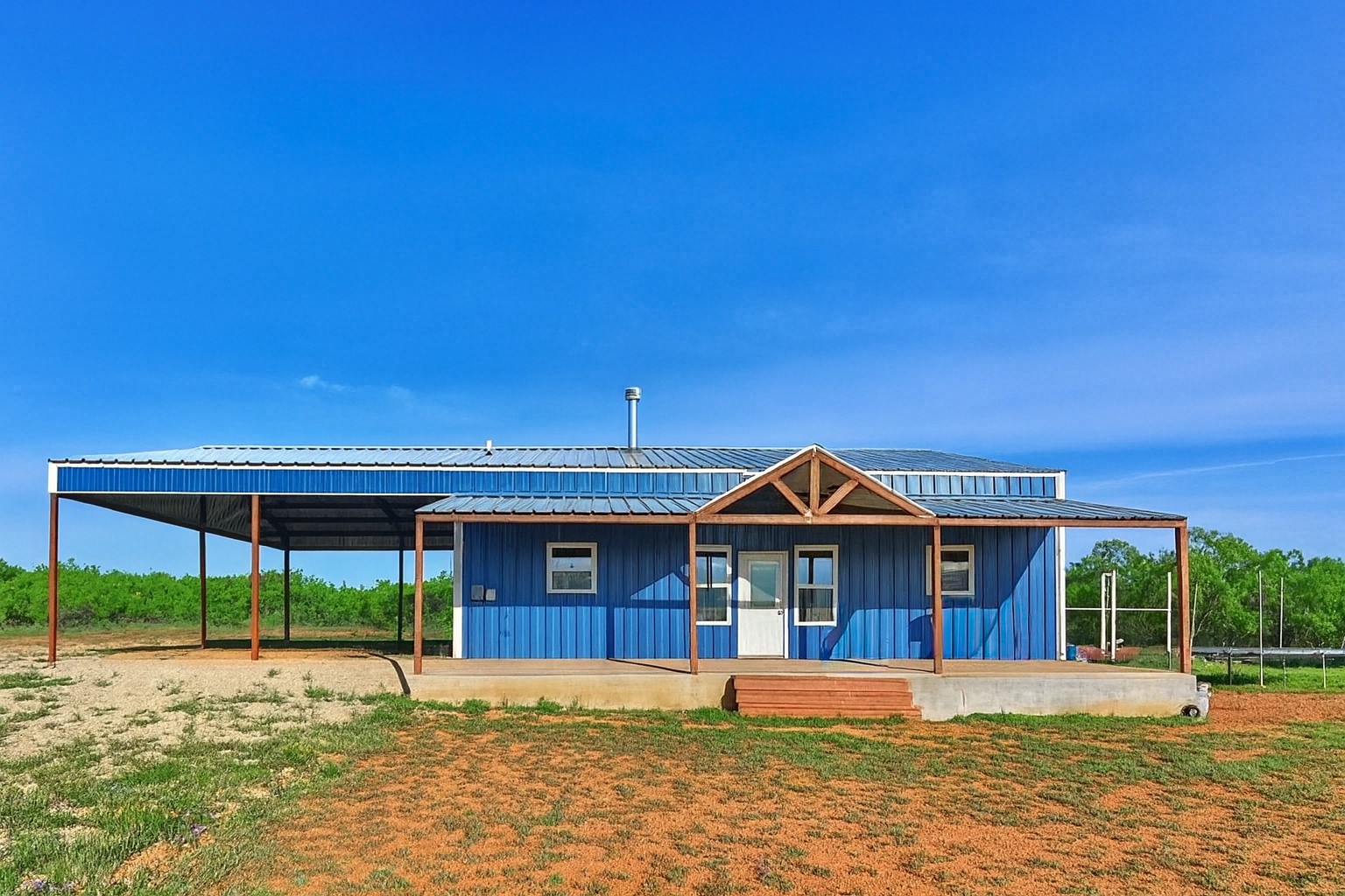 Blue metal-sided home with a timber-framed porch and large open-sided carport.