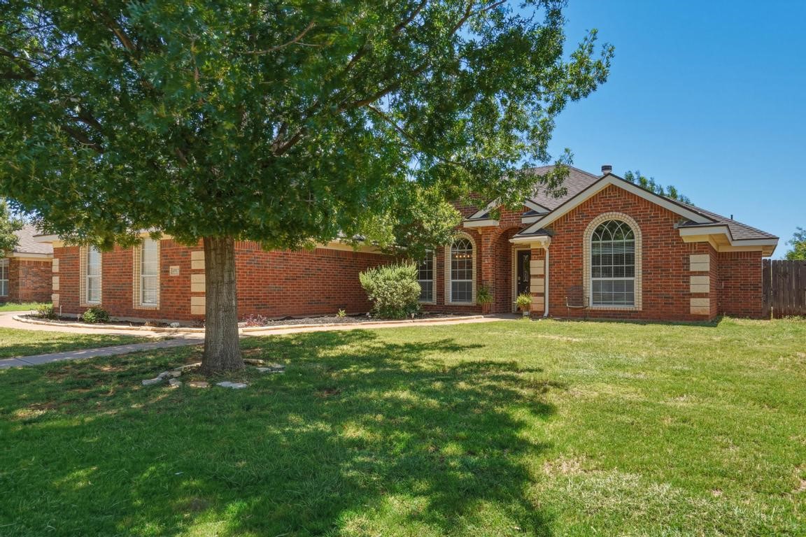 Single-story brick home with an arched front window, broad lawn, and large shade tree.