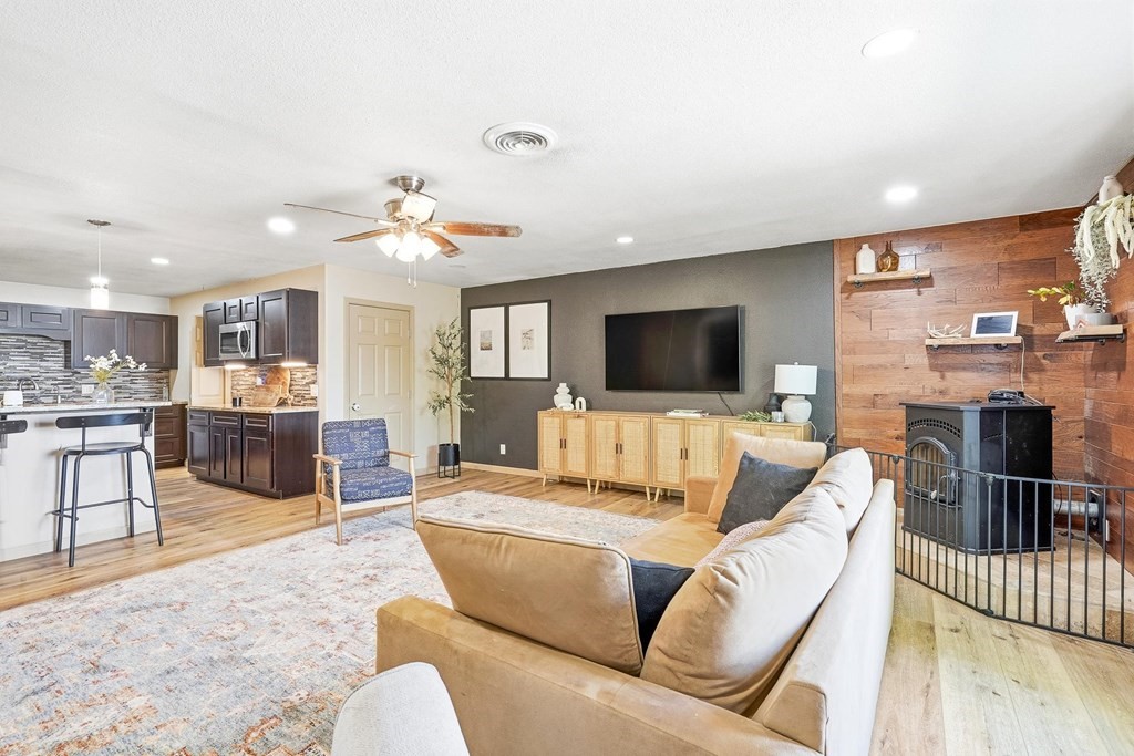 Open-plan living room with a beige sectional, dark kitchen cabinetry, and a fireplace on a wood accent wall.