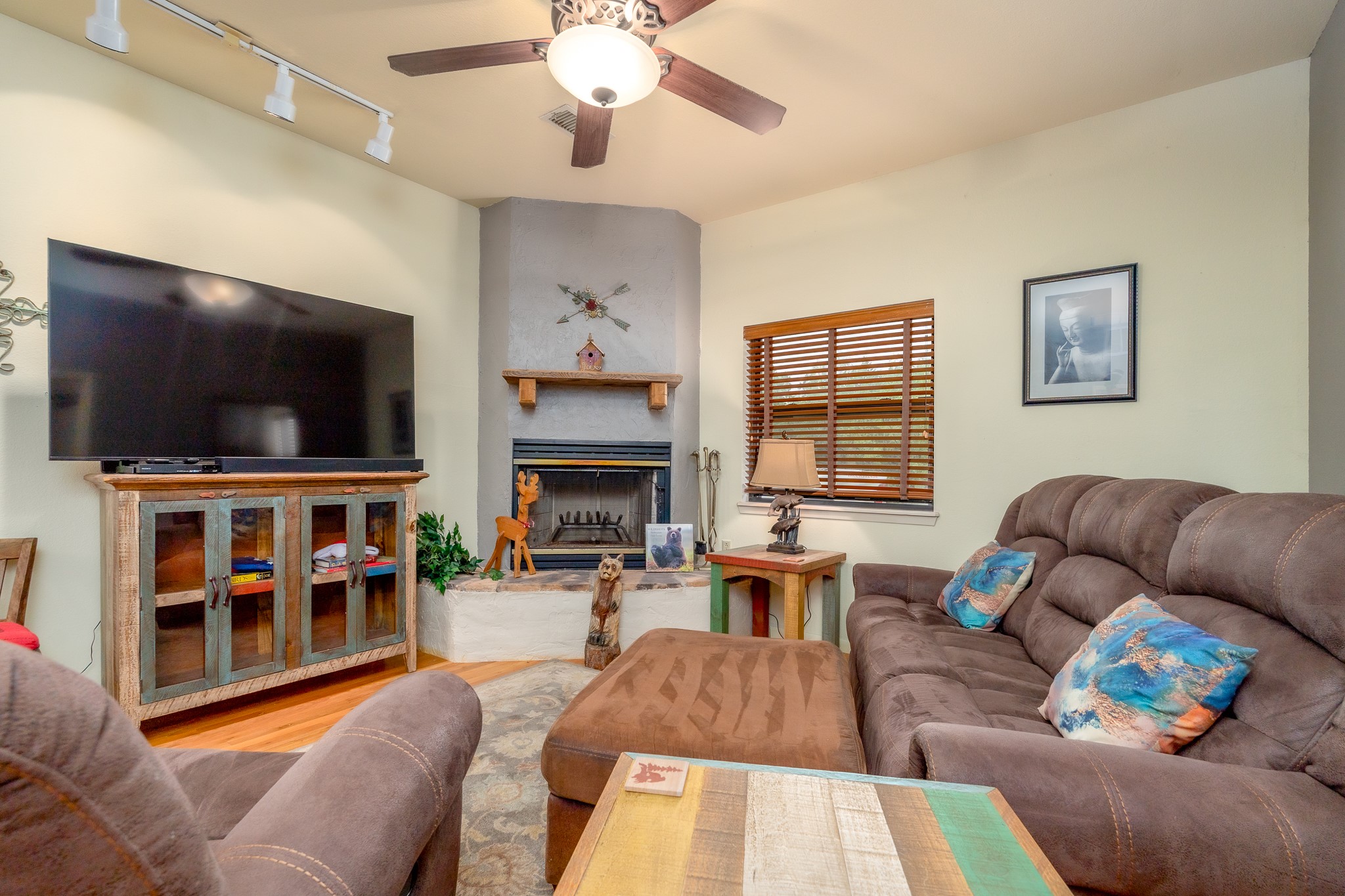 Living room with a corner fireplace, gray sectional, large television, and wooden blinds.