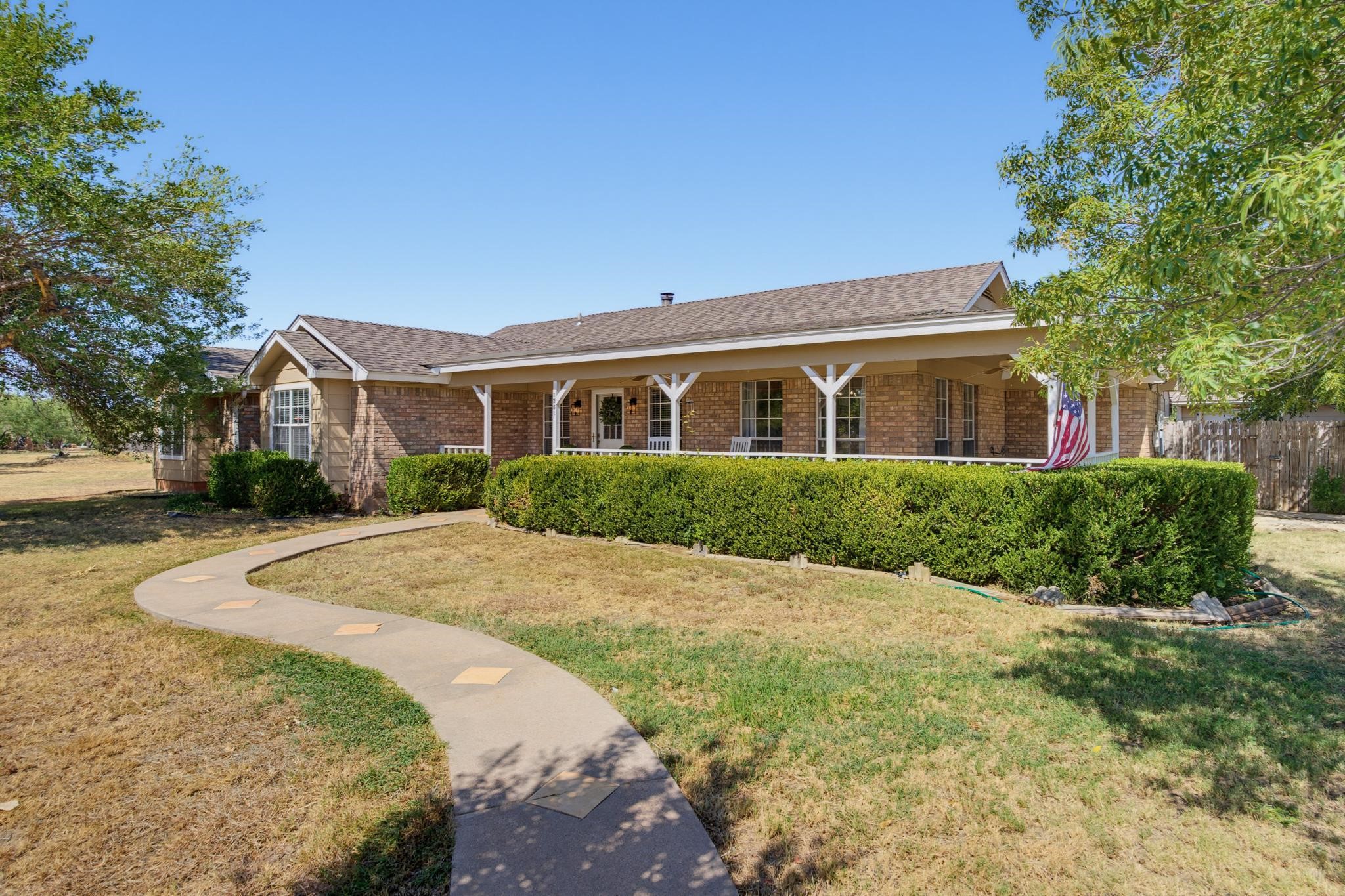 Brick ranch-style home with a long covered porch, clipped hedges, and a curved front walkway.